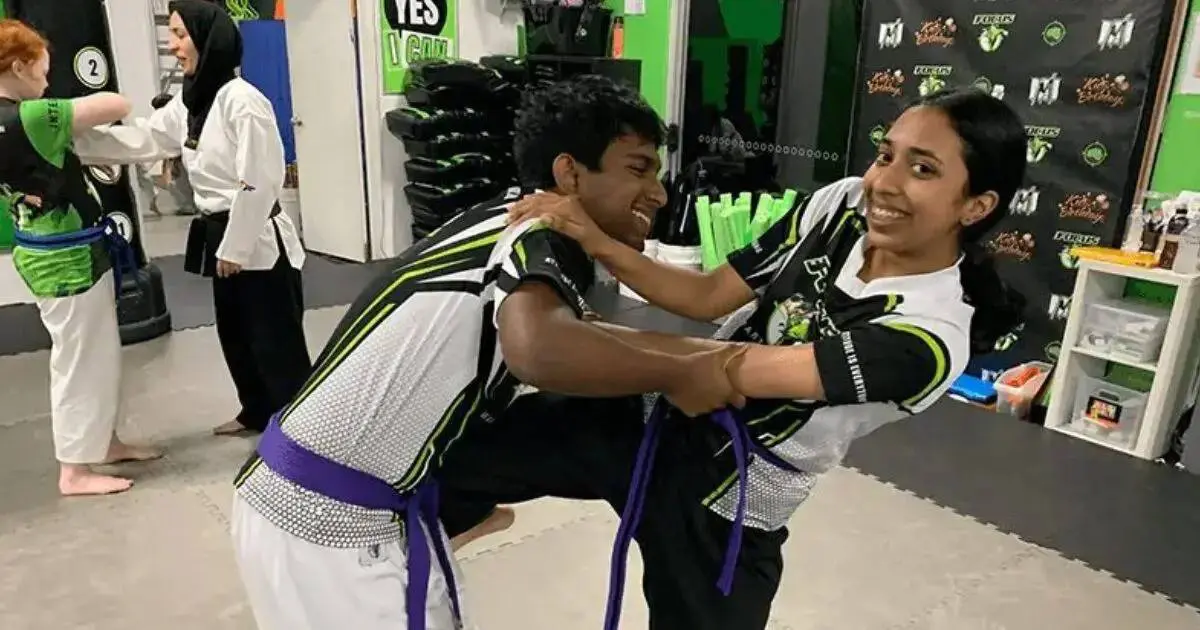 Two students practicing Brazilian jiu jitsu grappling techniques under instructor supervision