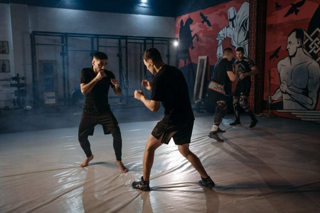 Two students facing off in a sparring stance while others train in the background, showing self defence fundamentals for beginners.